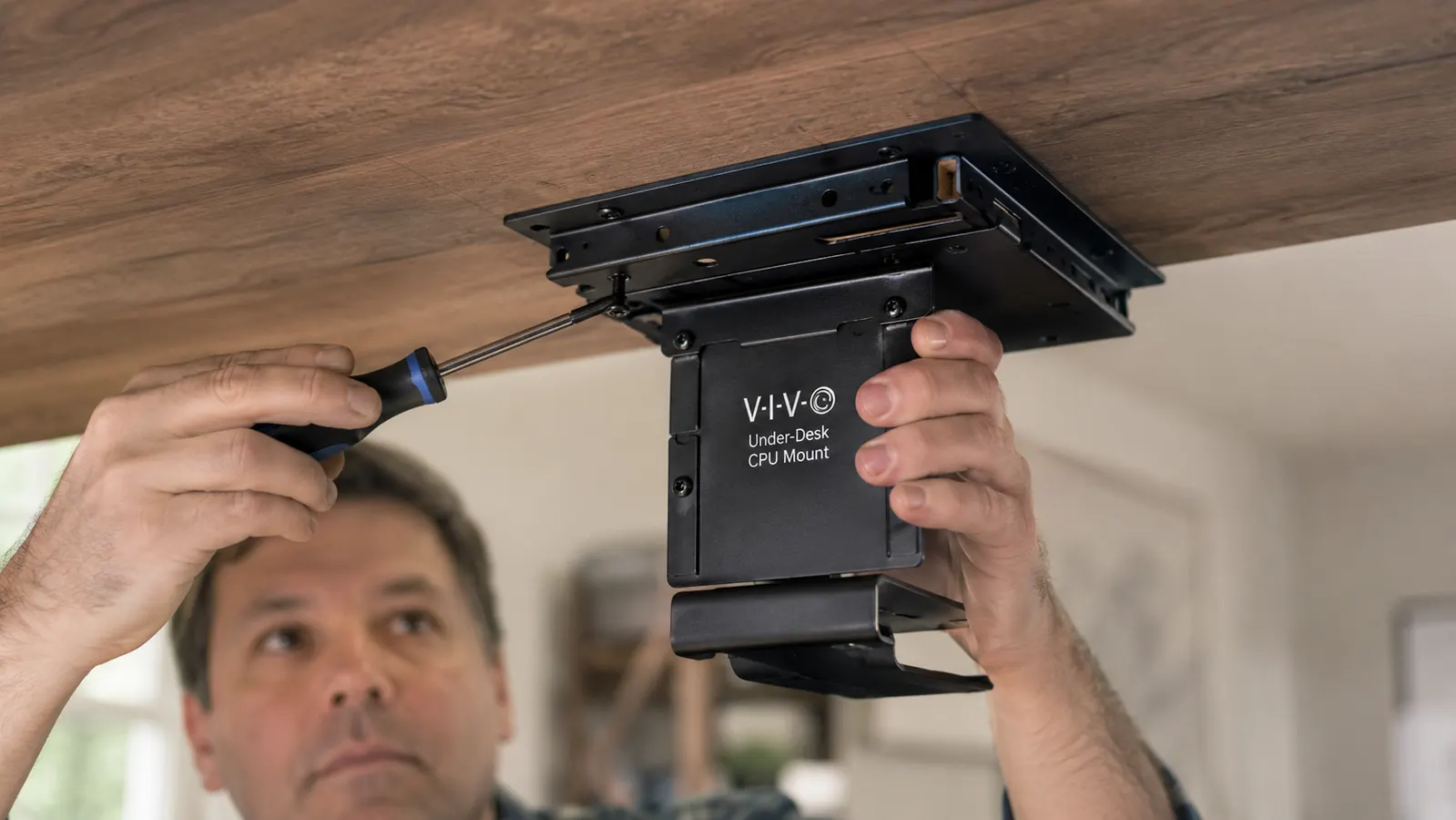Close-up of a hand screwing a metal mounting track into the underside of a wooden desk