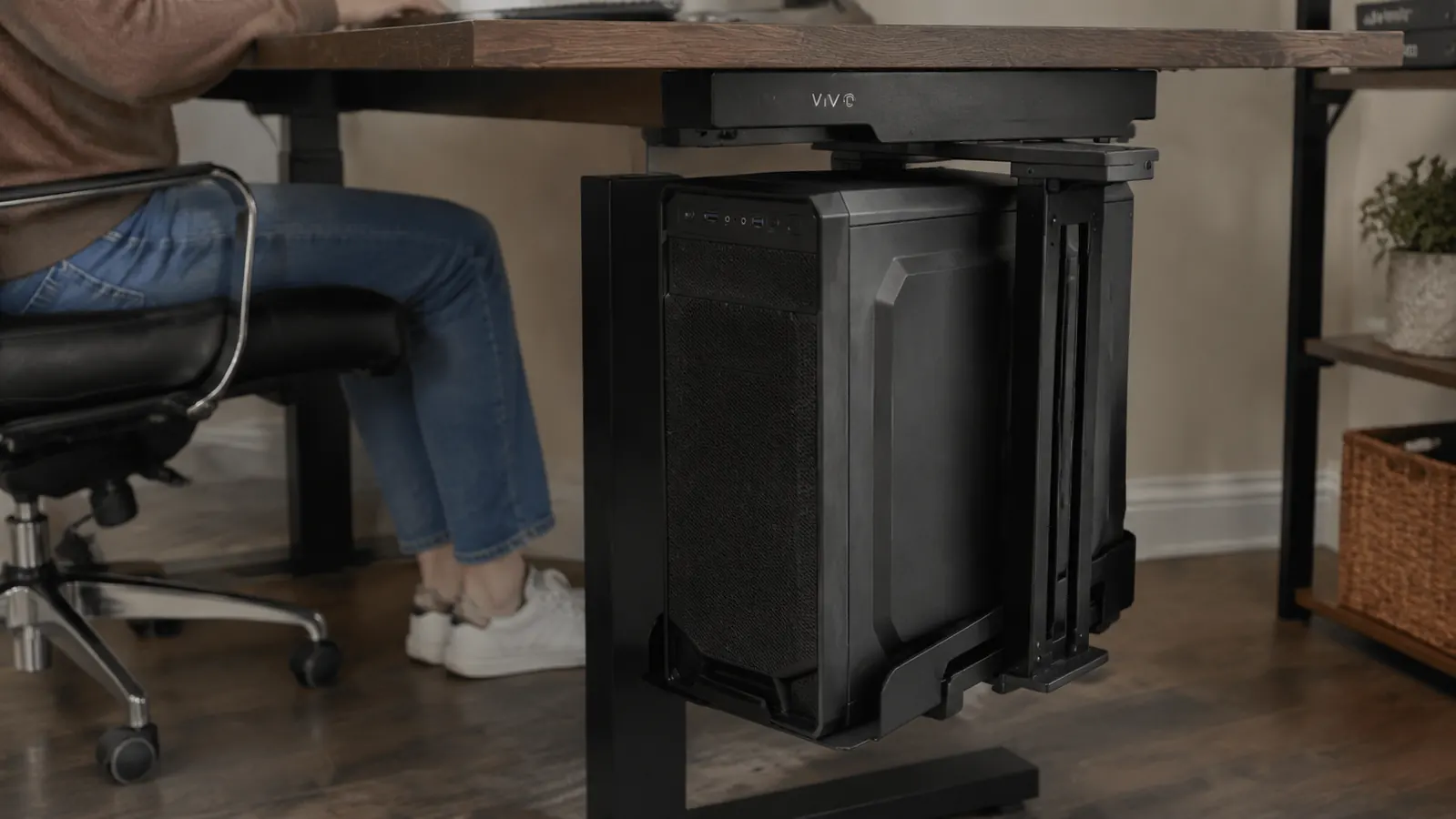 A desktop computer tower loaded into an adjustable under-desk mount cradle, swiveled partway out from under the desk