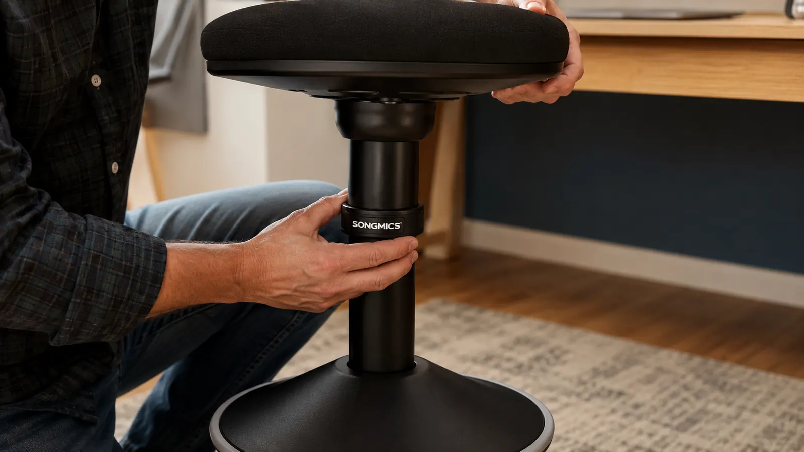 Hand adjusting the height collar on the pole of a black wobble stool before sitting down