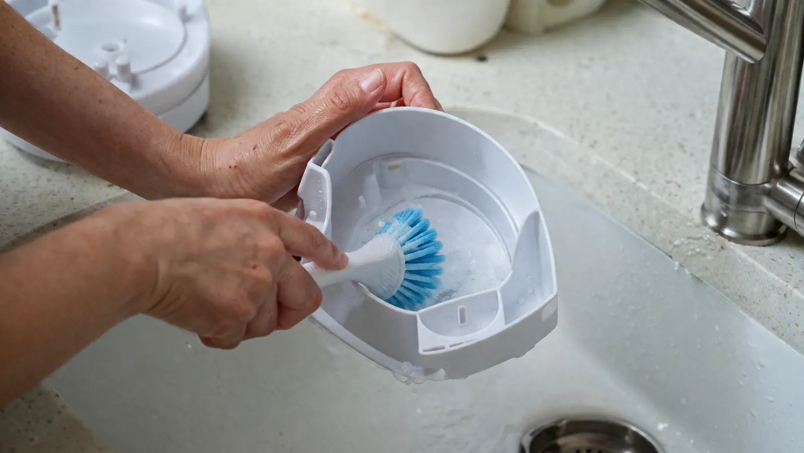 Close-up of a humidifier tank being cleaned with a soft brush and a vinegar water solution in a sink