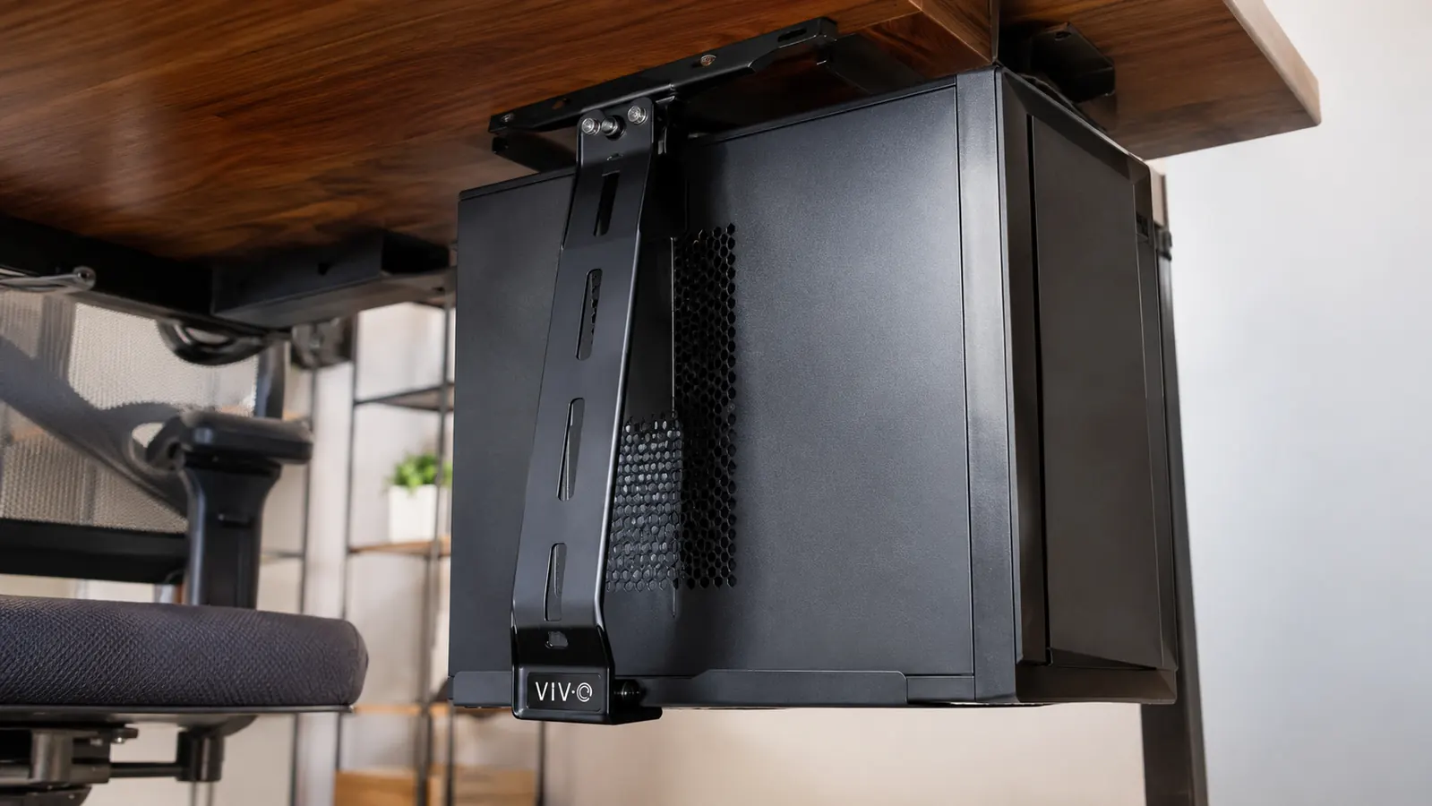 Close-up of a black steel CPU mount bracket holding a computer tower against the underside of a desk