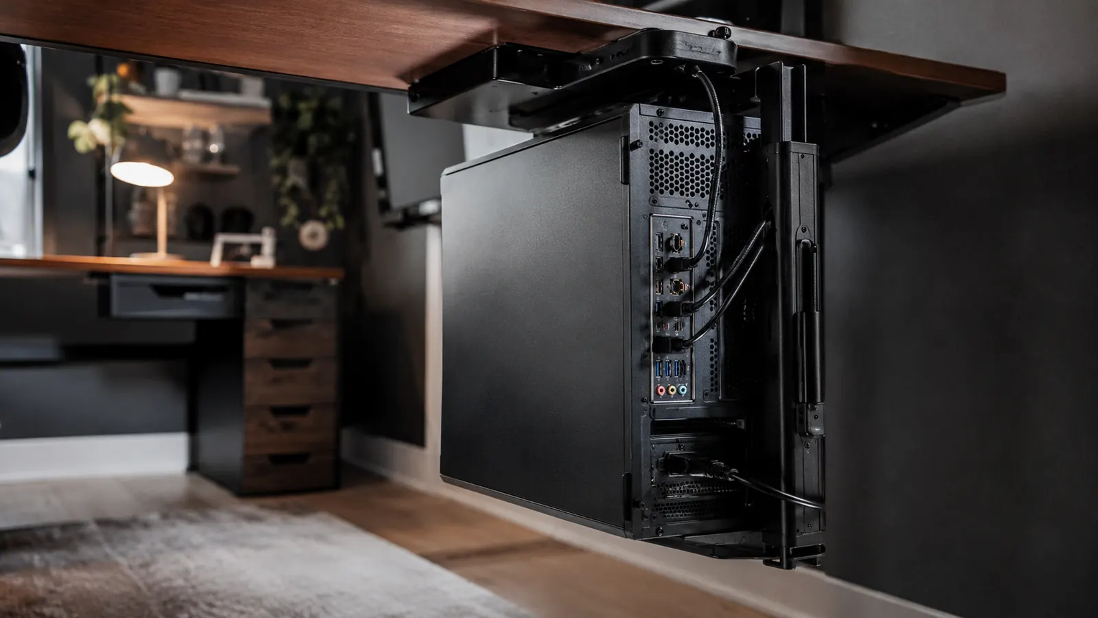 Underside of a home office desk showing a mounted CPU bracket swiveled fully out from beneath the desktop for access to the ports