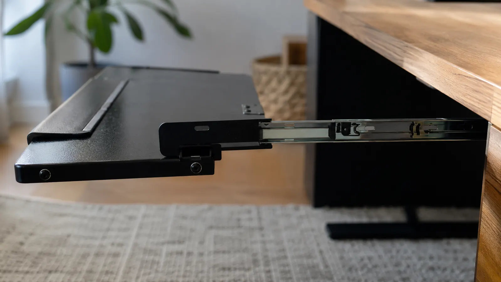 Side view of a keyboard tray extended to its full length beneath a desk, showing the sliding rail mechanism